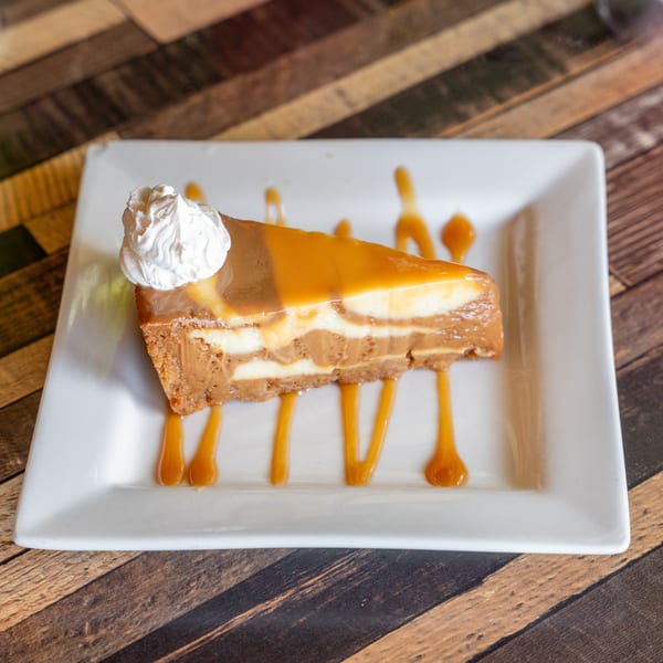 Slice of caramel cheesecake with whipped cream and caramel drizzle on a white plate.