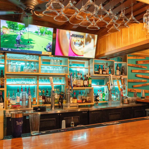 A well-stocked bar with bottles, glasses, beer taps, and TVs showing sports and entertainment.