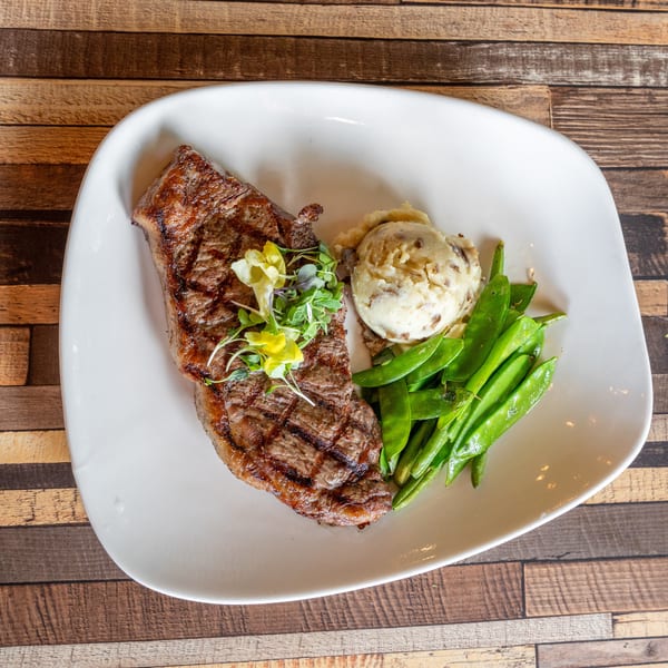 Grilled steak with mashed potatoes, snap peas, and microgreens on a white plate.