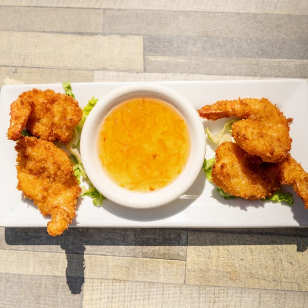 Crispy fried shrimp with a side of sweet chili sauce on a white rectangular plate.