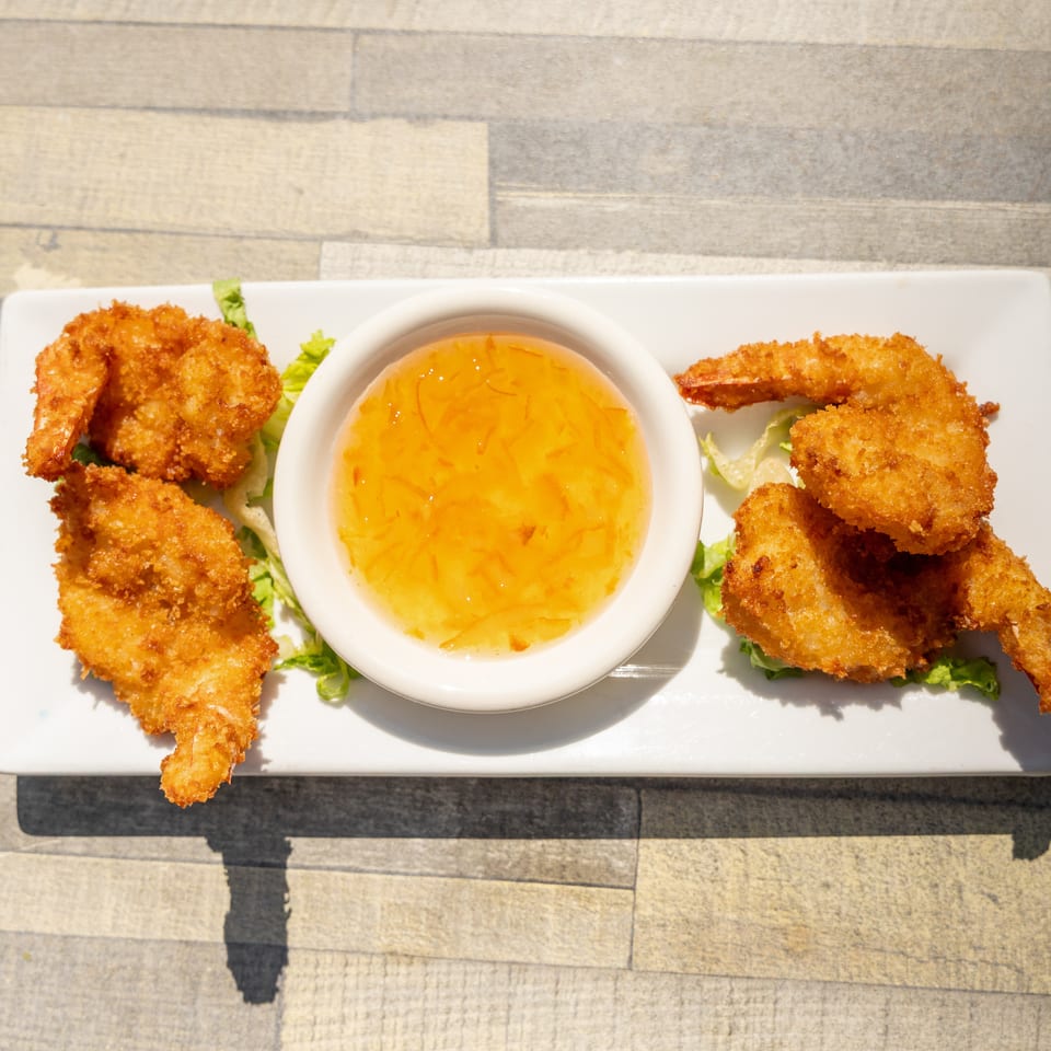 Crispy fried shrimp with a side of sweet chili sauce on a white rectangular plate.