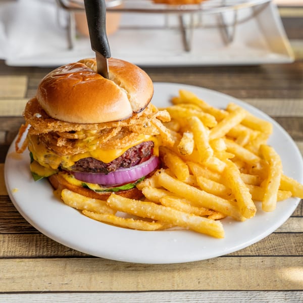 A cheeseburger with onion rings and a knife through it, served with a side of french fries.