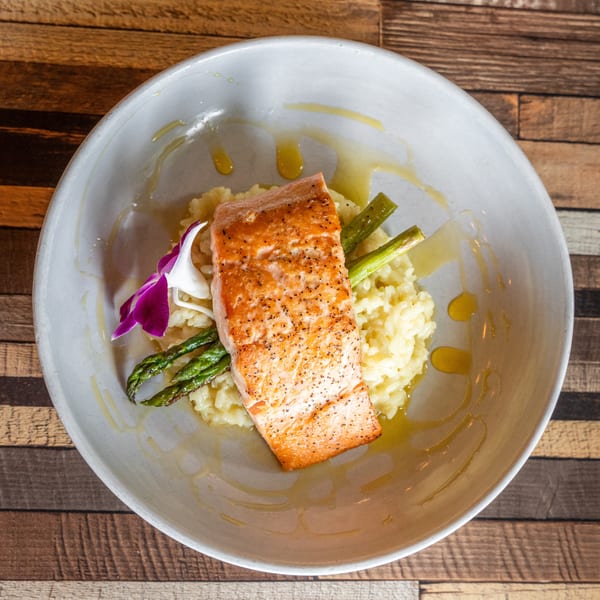Pan-seared salmon with asparagus and risotto, garnished with a purple orchid, in a white bowl.