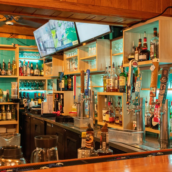 A well-stocked bar with various liquor bottles, beer taps, and two TVs showing sports.