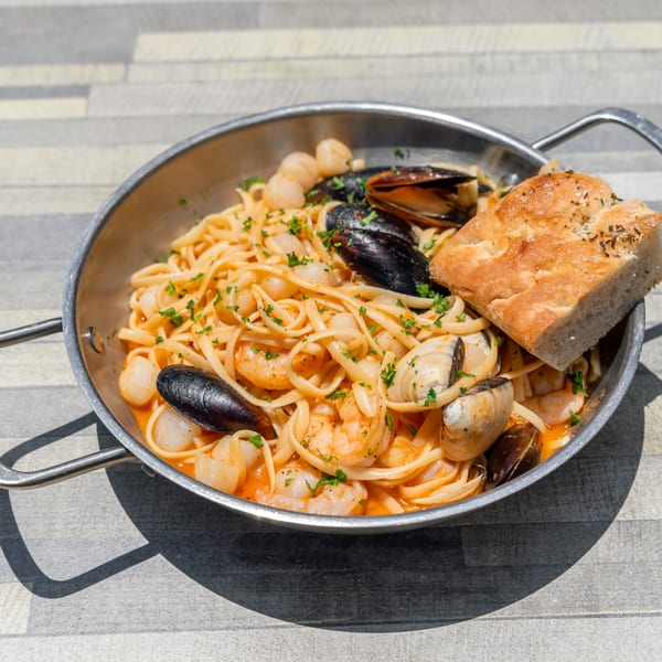 Seafood linguine with mussels, clams, shrimp, and scallops in a metal pan with focaccia bread.