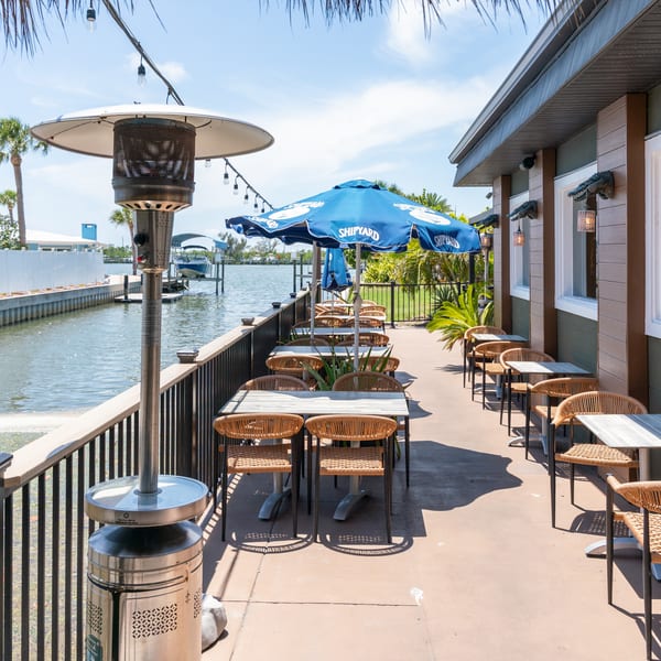 Outdoor patio dining area with tables, chairs, umbrellas, and a heater next to a canal.