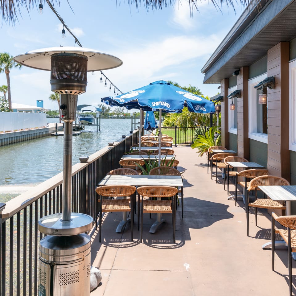 Outdoor patio dining area with tables, chairs, umbrellas, and a heater next to a canal.