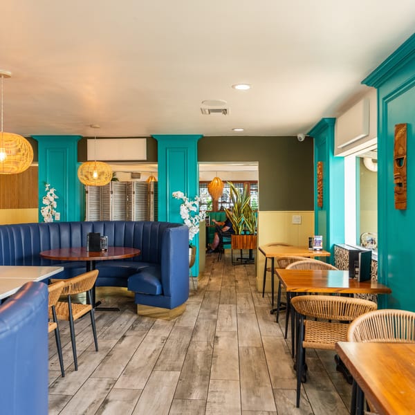 Restaurant interior with blue booths, wooden tables, wicker chairs, and teal accents on the walls.