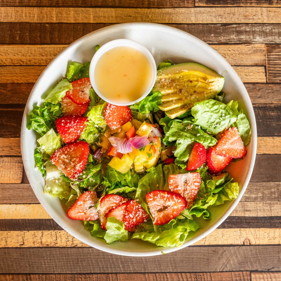 Fresh green salad with sliced strawberries, avocado, pineapple salsa, and dressing in a white bowl.