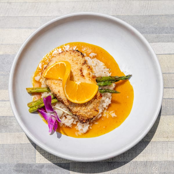 Crispy breaded fish with orange slices, asparagus, rice, and orange sauce on a white plate.